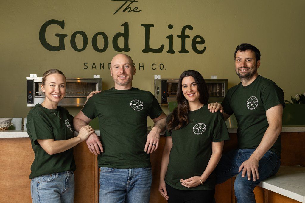 Marlo, Austin, and the Good Life team in green shirts in front of the shop's wall sign